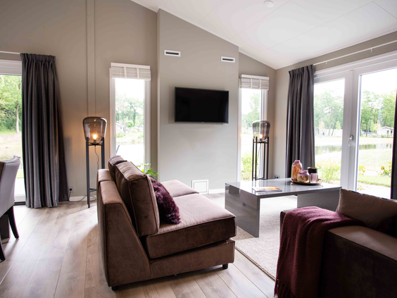 De sfeervolle woonkamer met een comfortabele zithoek, televisie en grote ramen in een vakantiehuis op Recreatiepark Beekbergen.