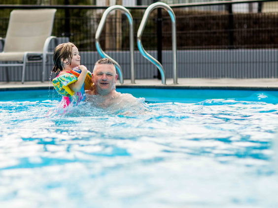 Een gezin met jonge kinderen heeft waterpret in het zwembad van Recreatiepark Beekbergen, omringd door ligstoelen.