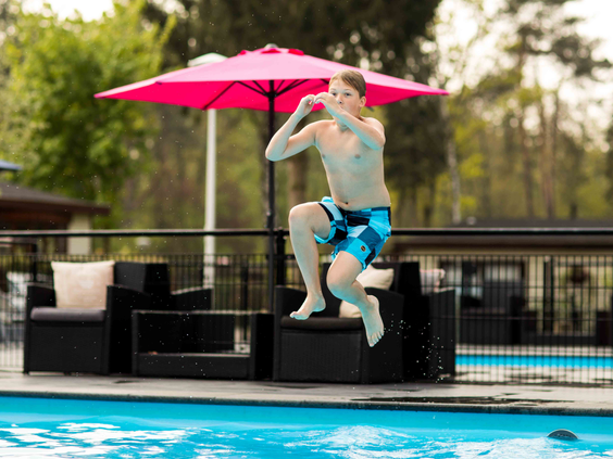 Een jongen springt met een grote sprong in het buitenzwembad van Recreatiepark Beekbergen en maakt een bommetje.