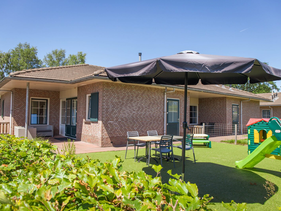 Een luxe bungalow op Recreatiepark de Boshoek met een omheinde tuin, terras met parasol en een privé-speeltoestel met glijbaan voor de kinderen.