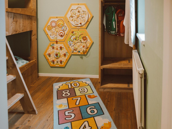 Een speels ingerichte kinderslaapkamer in een accommodatie op Recreatiepark de Boshoek, met een hinkelbaan op de vloer en spelletjes aan de muur.