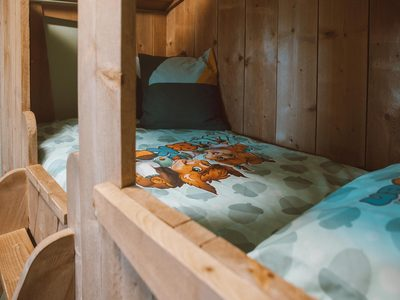 Een knusse, houten bedstee in een kinderkamer op Recreatiepark de Boshoek, opgemaakt met vrolijk kinderbeddengoed.