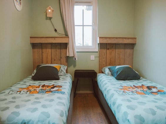 Een kinderslaapkamer met twee aparte bedden en beddengoed met daarop de mascottes van Recreatiepark de Boshoek, Kees en Eva de eekhoorns.