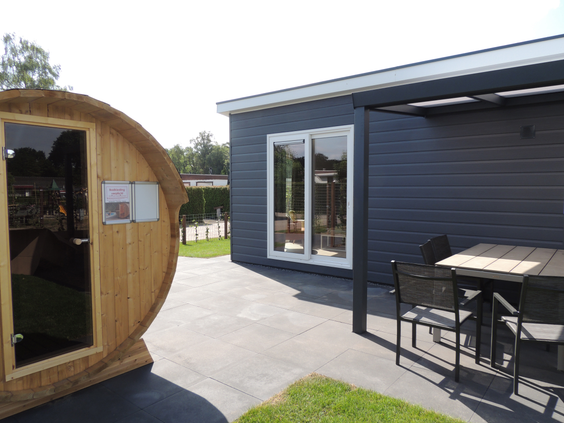 De buitenkant van een luxe wellness-accommodatie op Recreatiepark de Boshoek, met een privé barrelsauna op het terras.