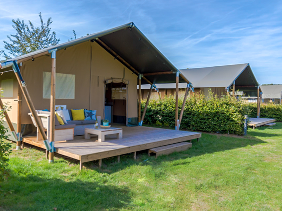 De buitenkant van een luxe safaritent op Recreatiepark de Boshoek, met een comfortabele loungeset op de ruime houten veranda.