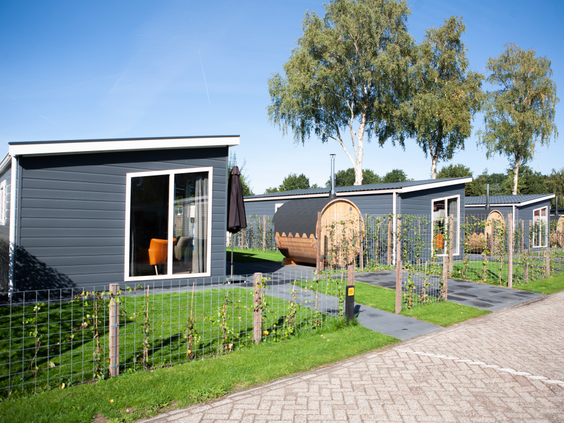 Een straatje met moderne vakantiehuisjes op Recreatiepark de Boshoek, met privé tuintjes en een houten barrelsauna.