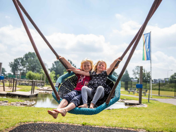 Twee meisjes hebben samen plezier op de grote vogelnestschommel in de speeltuin van Recreatiepark Het Esmeer.