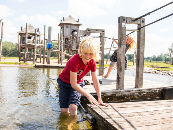 Een jongen speelt op de rand van een houten vlot in het water bij het avontuurlijke speeleiland van Recreatiepark Het Esmeer.