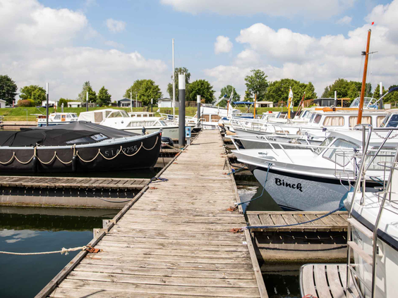 De houten steiger in de jachthaven van Recreatiepark Het Esmeer, met diverse aangemeerde plezierjachten en zeilboten.
