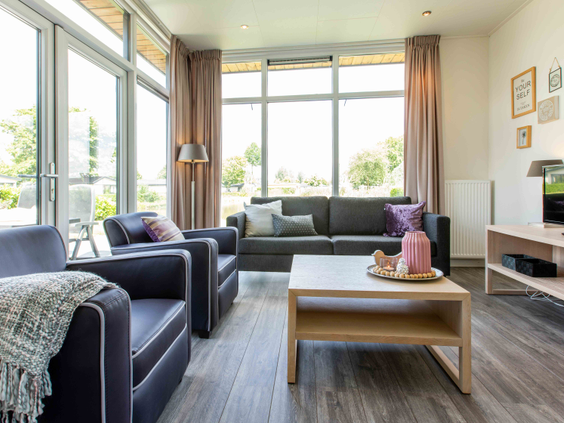 Lichte en moderne woonkamer met grote ramen in een vakantiehuis op Recreatiepark Het Esmeer, ingericht met een comfortabele bank en stoelen.