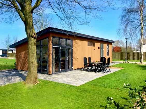 De buitenkant van een modern vakantiehuisje met een groot terras en tuinmeubilair, gelegen in het groen van Recreatiepark Het Esmeer.