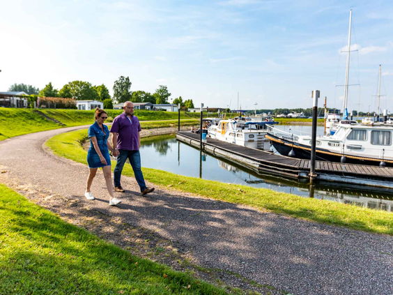 Een ouder wandelt met een kind hand in hand over het pad langs de jachthaven vol met boten bij Recreatiepark Het Esmeer.