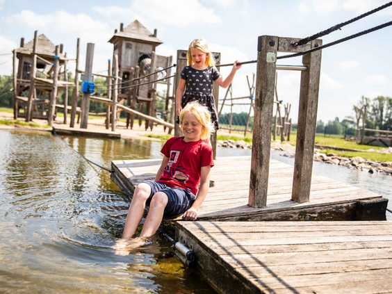 Kinderen spelen op een houten vlot bij het avontuurlijke speeleiland en poedelen met hun voeten in het water van het Esmeer.