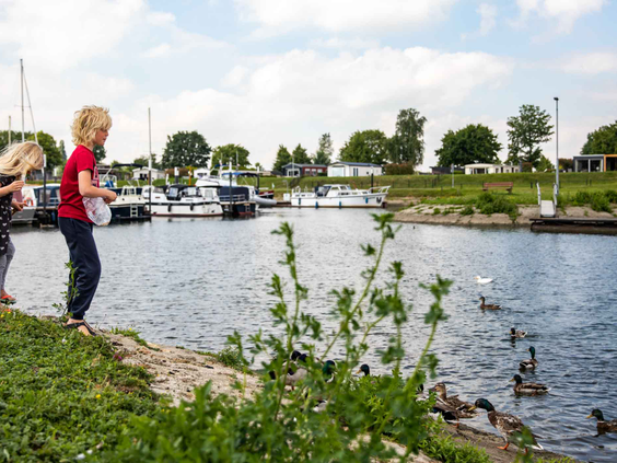 Kinderen kijken vanaf de kant naar de plezierjachten en bootjes die in de jachthaven van Recreatiepark Het Esmeer liggen.