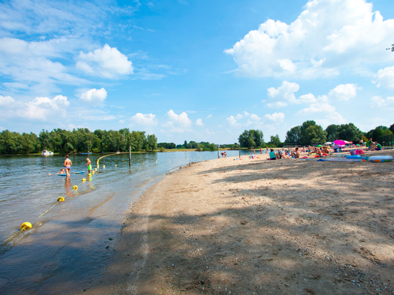 Het brede zandstrand aan recreatieplas het Esmeer, waar kinderen in het water spelen op een zonnige dag.