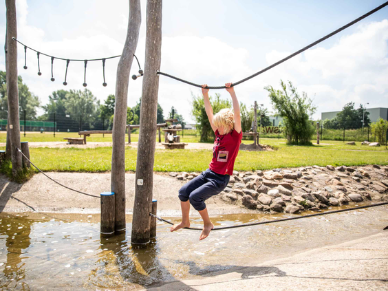 Een jongen slingert als een aapje aan een touw over het water in de avontuurlijke waterspeeltuin van Het Esmeer.