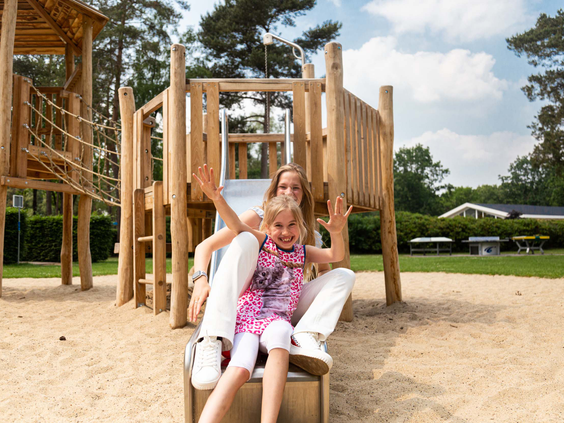 Meisje zit op een houten speeltoestel in de buitenlucht op Recreatiepark 't Gelloo.