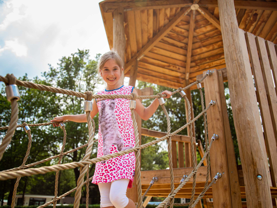 Meisje balanceert over een houten touwbrug in de speeltuin van Recreatiepark 't Gelloo.