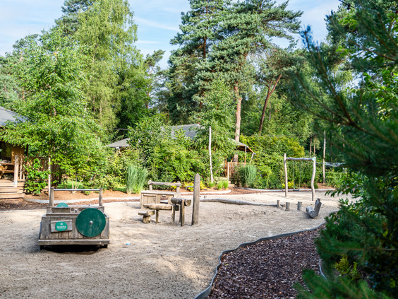 Ruime zandspeeltuin met schommels en houten speeltoestellen op Recreatiepark 't Gelloo.