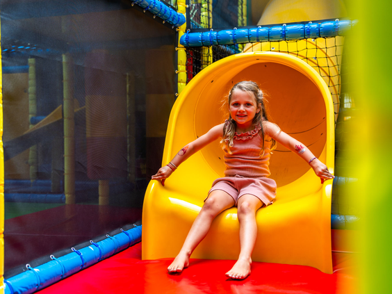 Meisje glijdt van de gele glijbaan in de overdekte binnenspeeltuin van Recreatiepark 't Gelloo.