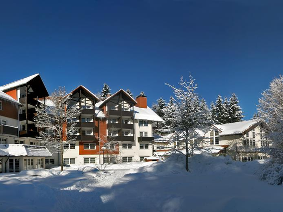 Het Relexa Hotel in Braunlage, gelegen in een prachtig winters landschap met veel sneeuw en bomen onder een helderblauwe hemel.