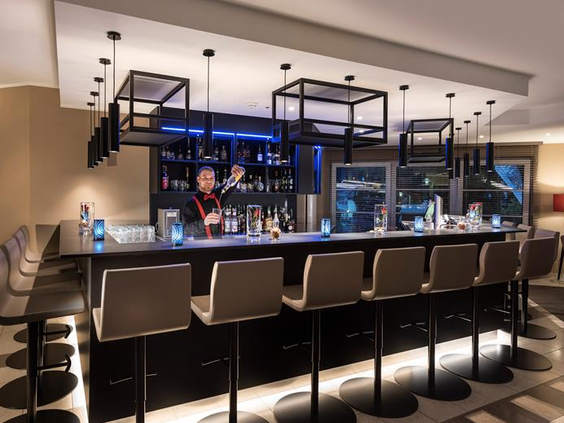 De moderne en sfeervol verlichte hotelbar van het Relexa Hotel in Braunlage, waar een barman drankjes bereidt.