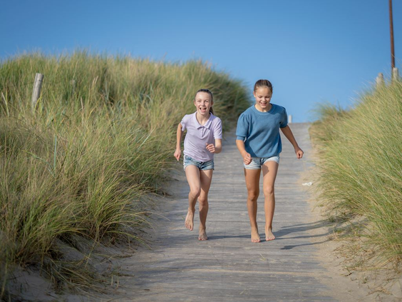 Twee kinderen rennen op blote voeten een duinpad af richting het strand bij Bergen, Noord-Holland.