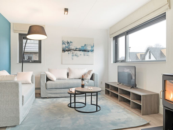 De moderne, lichte woonkamer van een vakantievilla op Residence Berger Duinen, met een comfortabele zithoek en open haard.