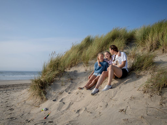 Een gezin zit te genieten in het zand van een duin bij het strand van Bergen aan Zee.