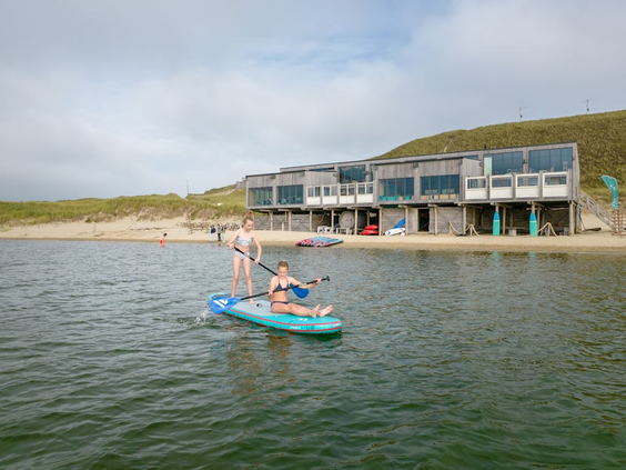 Twee kinderen aan het suppen (stand-up paddling) op het water voor de moderne appartementen van Residence Berger Duinen.