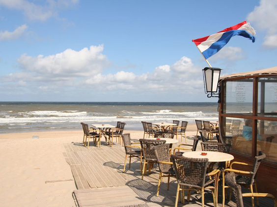 Een zonnig terras van een strandpaviljoen in Bergen aan Zee, met uitzicht op het strand en de golven van de Noordzee.
