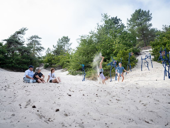 Kinderen en gezinnen spelen in het mulle zand en op speeltoestellen in de speelkuil van de Schoorlse Duinen.
