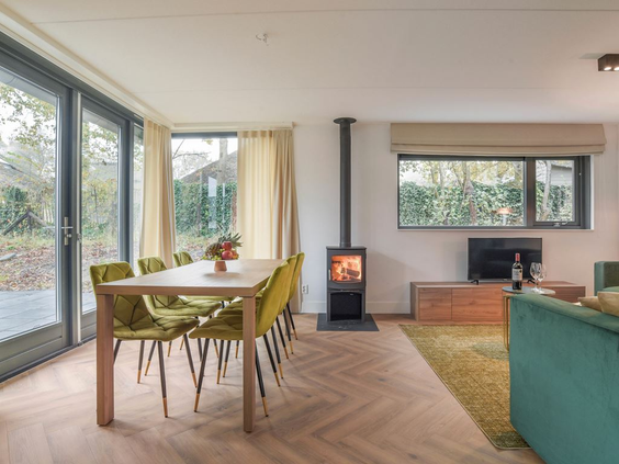 De lichte, moderne woonkamer met eethoek en gezellige houtkachel in een vakantiehuis op Residence Berger Duinen.