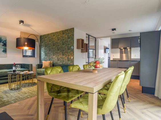 De stijlvolle eethoek met groene stoelen en de open keuken in een luxe vakantievilla op Residence Berger Duinen.