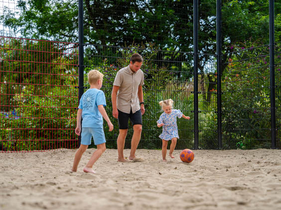 Kinderen en een volwassene spelen een potje voetbal op het grasveld bij de speeltuin van Residence Lichtenvoorde.