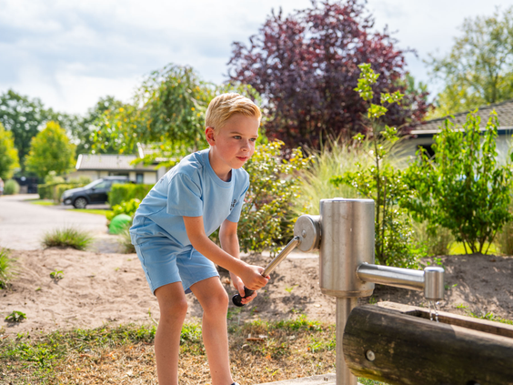Jongen speelt met een houten waterpomp in de natuurlijke speeltuin van Residence Lichtenvoorde.