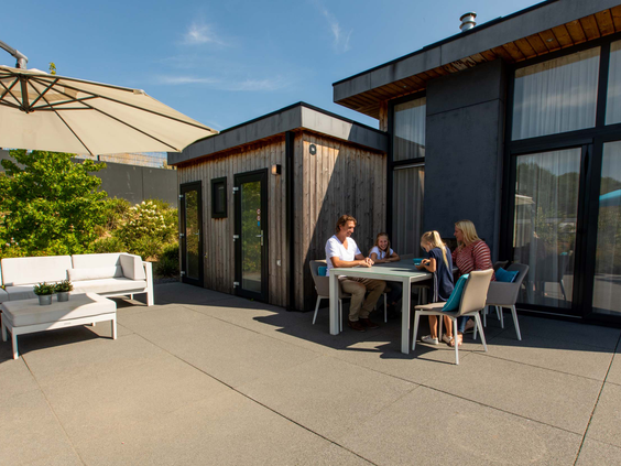 Een gezin geniet van een drankje op het zonnige terras van een Module Z vakantiewoning op Residence Valkenburg.