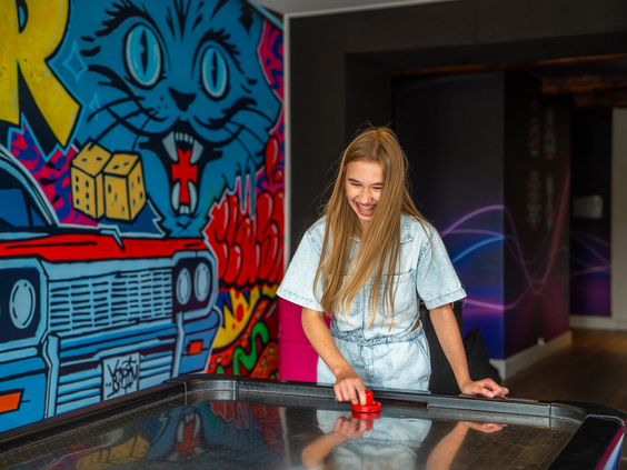Een meisje speelt een fanatiek potje airhockey in de modern ingerichte gameroom van Residence Valkenburg.