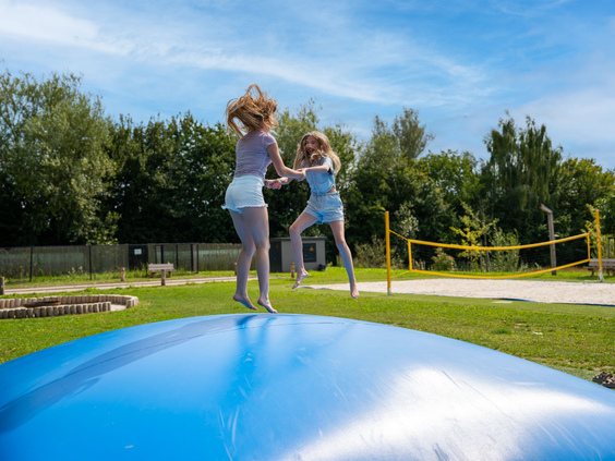 Meisjes springen en maken salto's op de grote air-trampoline op het speelveld van Residence Valkenburg.