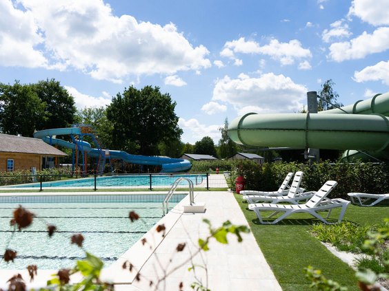 Overzicht van het buitenzwembad met waterglijbanen en ligbedden op de ligweide bij Resort Kaatsheuvel in Noord-Brabant.