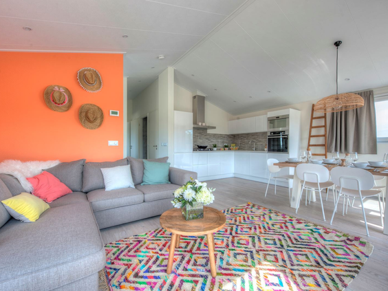 Overzicht van het lichte en open interieur van een vakantiehuis, met een moderne keuken en een sfeervolle woonkamer met oranje accentmuur.