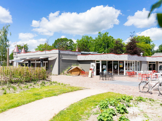 Het centrumgebouw van Resort Kaatsheuvel met een terras, een moestuin en een pad dat naar de ingang leidt.