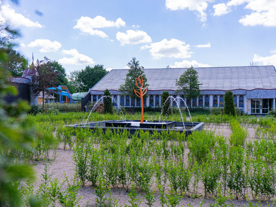 tuin met spuitende fonteinen en een oranje sculptuur in het midden op Resort Kaatsheuvel.