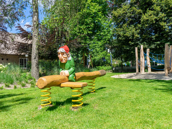 Een grappig veertoestel in de vorm van een kabouter op een boomstam in de speeltuin van Resort Kaatsheuvel.