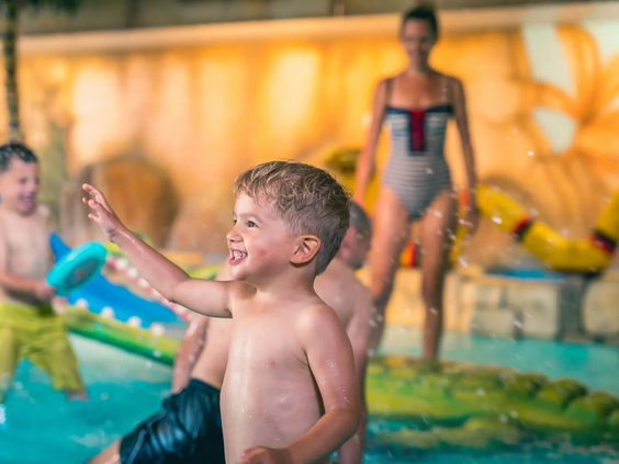 Lachende jongen spettert vrolijk in het binnenzwembad van Resort Kaatsheuvel, omringd door speelelementen.