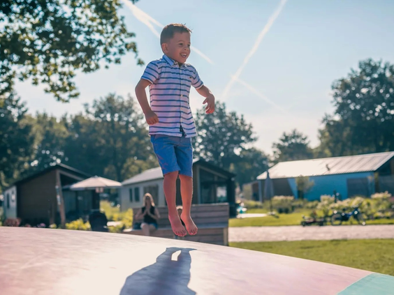 Een jongen maakt een hoge sprong op de grote air-trampoline van Resort Kaatsheuvel, met vakantiehuisjes op de achtergrond.