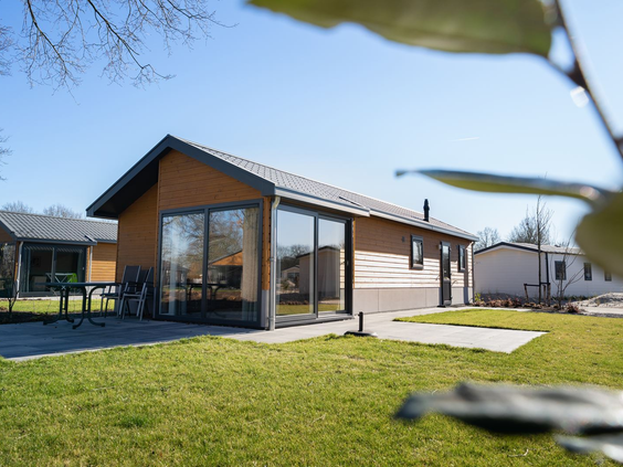 Een modern, houten vakantiehuis met grote ramen en een terras in een groene tuin op Resort Kaatsheuvel.
