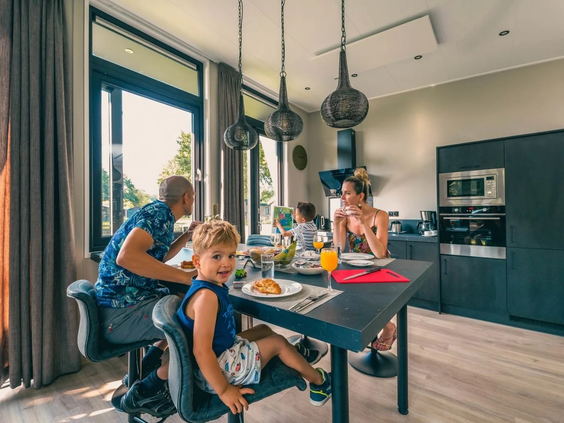 Een gezin met kinderen geniet van een maaltijd aan de grote eettafel in de moderne keuken van hun vakantiehuis op Resort Kaatsheuvel.