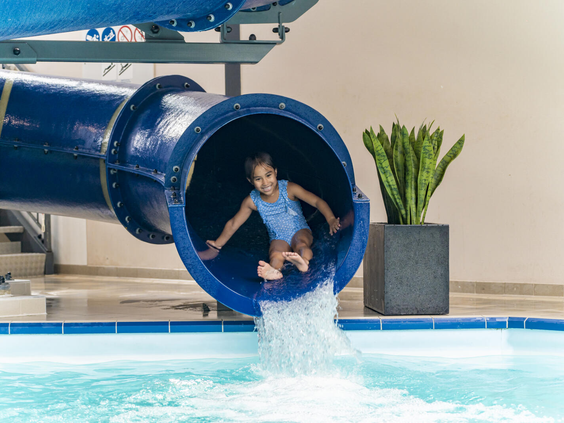Een meisje komt met een grote plons uit de blauwe waterglijbaan in het binnenzwembad van Dormio Resort Maastricht.