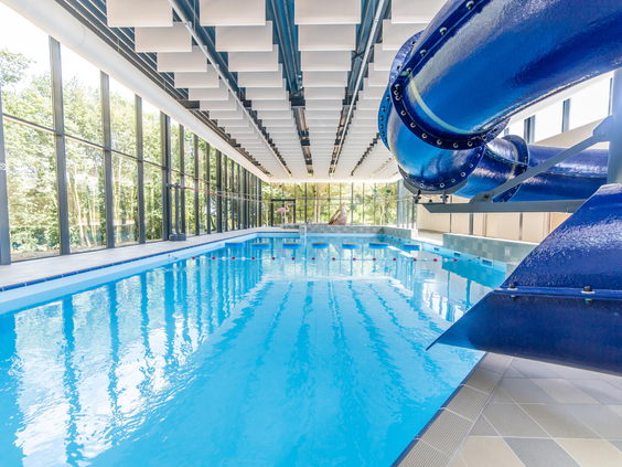 Het overdekte binnenzwembad van Dormio Resort Maastricht met een lange zwembaan en een grote blauwe waterglijbaan.